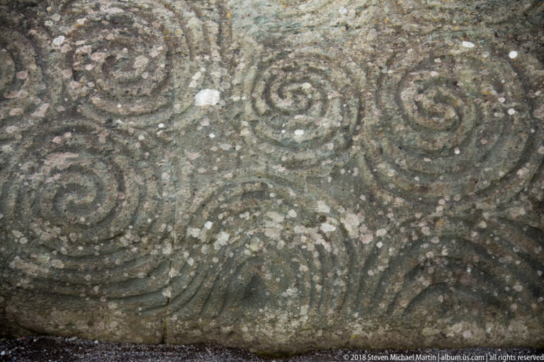 Close-up of multiple incised spiral motifs carved into a weathered stone at Newgrange.