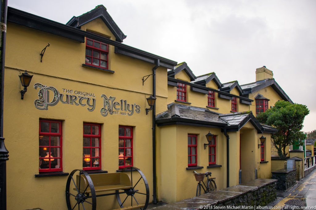 Yellow exterior of The Original Durty Nelly's with red windows, painted sign, lanterns, and a decorative cart.