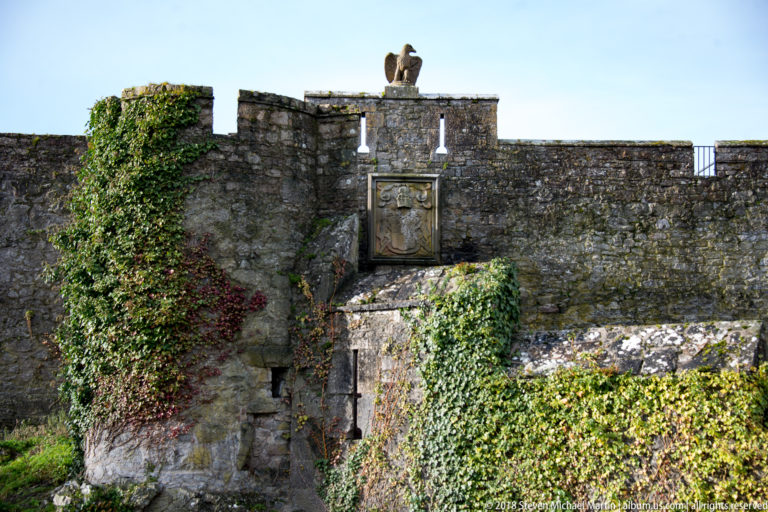Ivy-covered castle wall with a heraldic relief and small bird sculpture above the parapet.