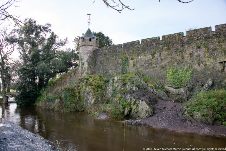 Small conical-roofed turret and crenellated stone wall above the river and exposed rock at Cahir Castle.