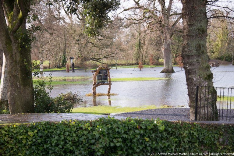 Floodwater surrounding trees and a wooden bench in landscaped grounds near Cahir Castle.