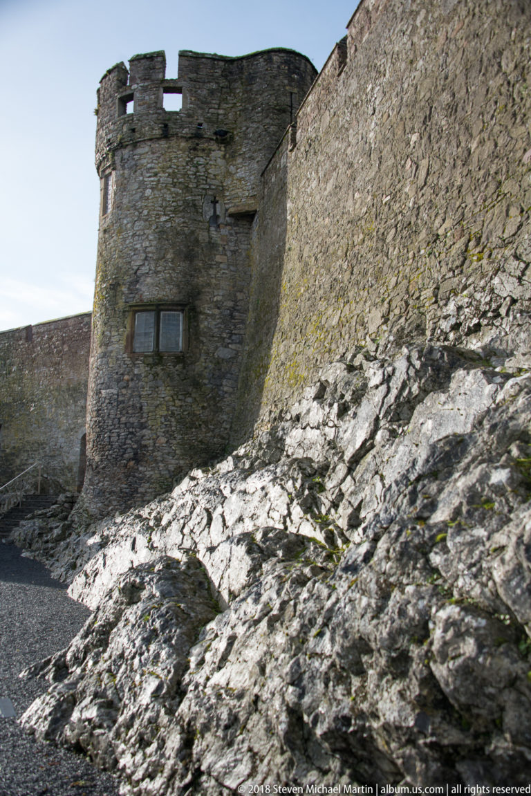 Thick stone castle walls built directly onto exposed gray bedrock, with a small rectangular opening.