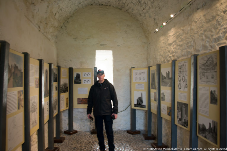 Visitor standing between rows of interpretive panels in a narrow vaulted stone room at Cahir Castle.
