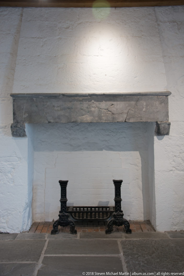 Black cast-iron grate centered in a broad whitewashed fireplace beneath a heavy stone lintel.