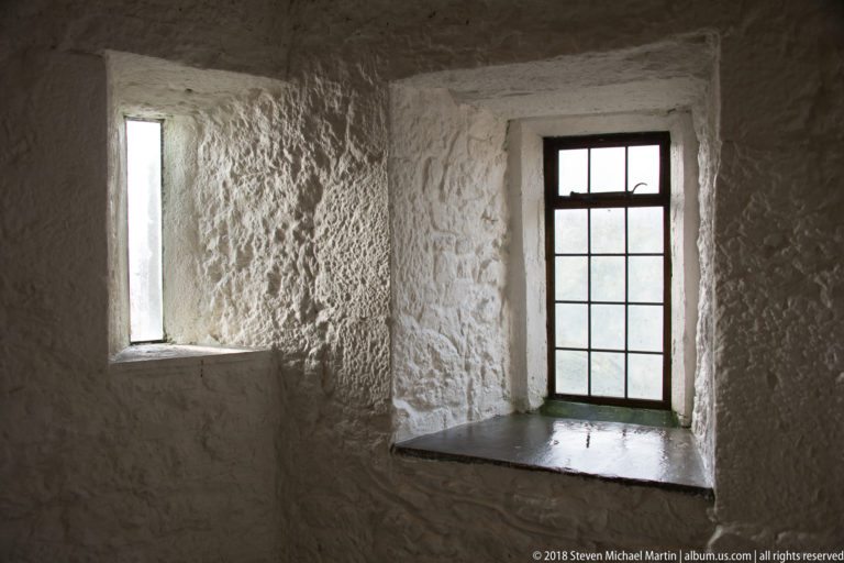 Two deep-set windows in a whitewashed stone corner, one narrow and one larger with dark mullions.