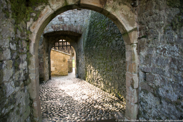 Sunlit cobbled passage framed by two successive stone arches within Cahir Castle.