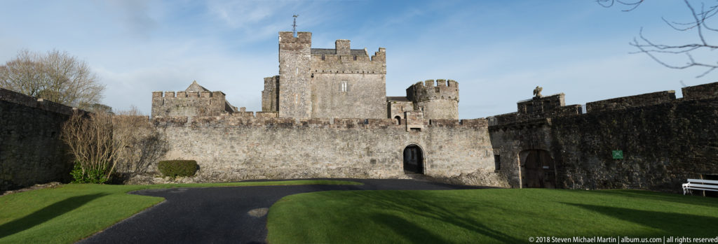 Broad lawn and path leading to Cahir Castle’s tall central tower, lower towers, and arched entrance.