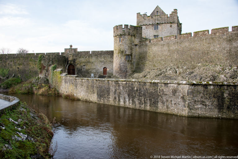 Long stone wall, round tower, and recessed entrance of Cahir Castle beside the River Suir.