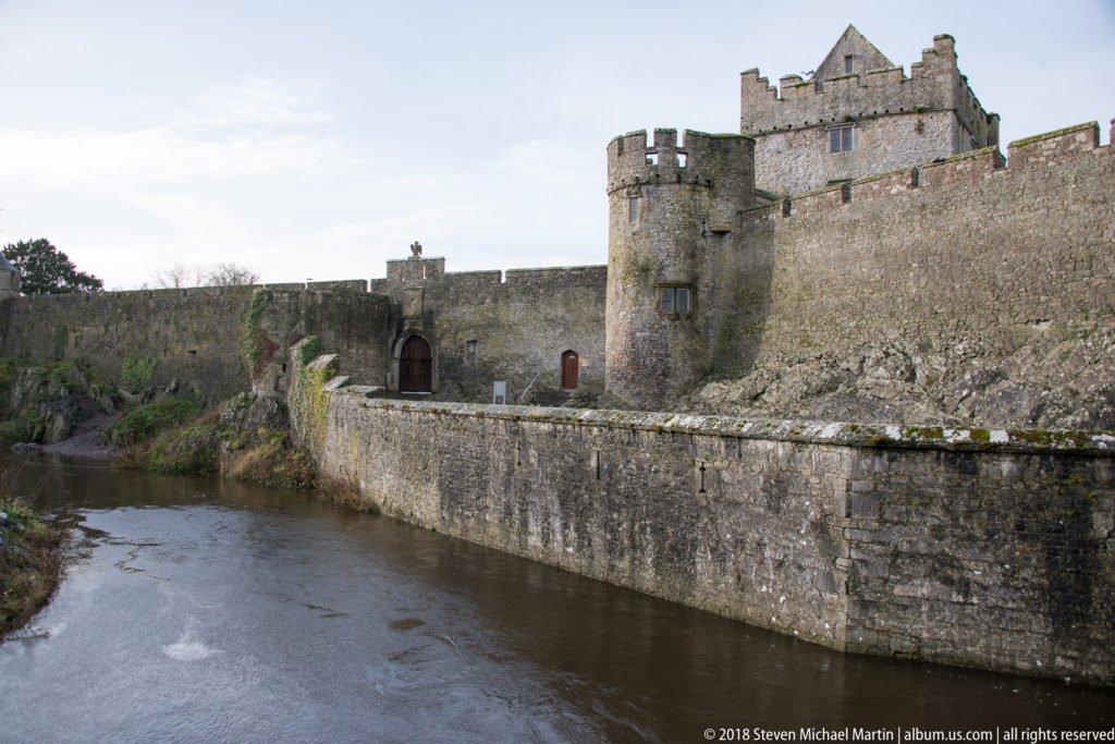 River channel below Cahir Castle’s high stone wall, round tower, and recessed gateway.