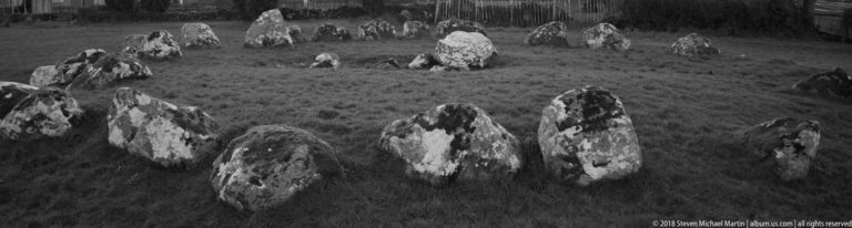 Black-and-white view from within a megalithic stone ring, with large foreground boulders and a taller stone beyond.