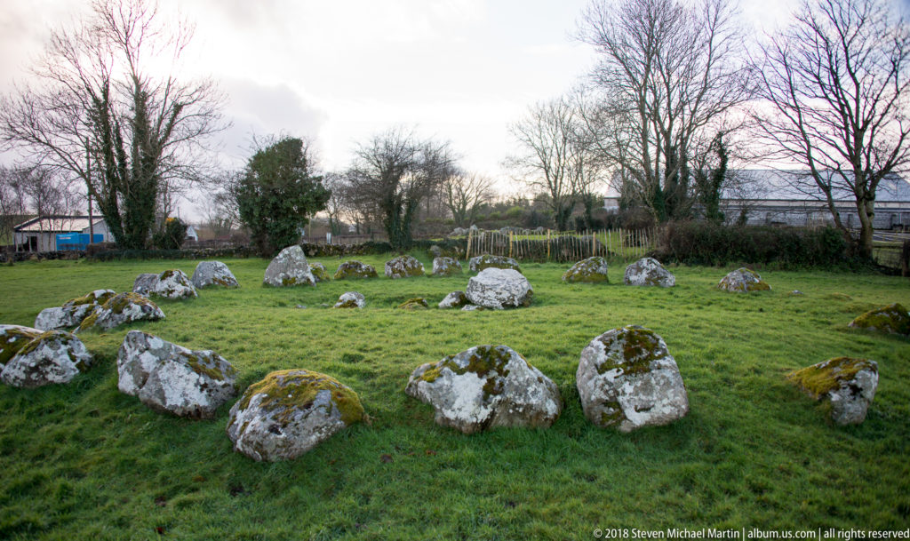 Broad circular arrangement of moss- and lichen-covered boulders across level green grass.