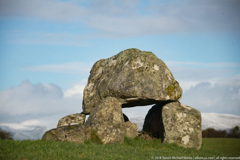 Close frontal view of a massive capstone over upright stones and a dark chamber opening.