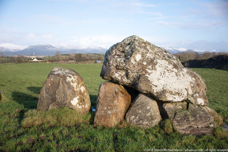 Frontal close view of a broad capstone supported by several weathered upright stones in pasture.