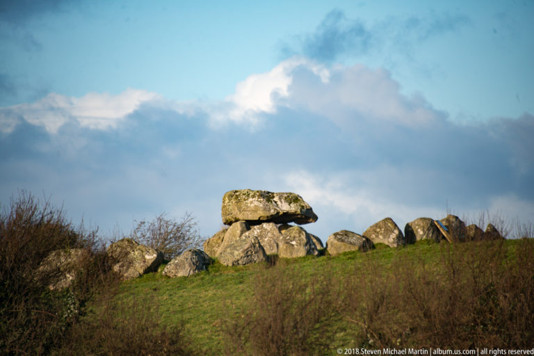 Large capstone resting on upright stones along a grassy ridge, with lower boulders extending beside it.