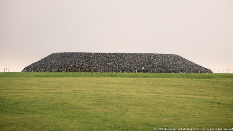 Closer profile of a broad stone cairn with densely packed stones and sloping sides above green pasture.