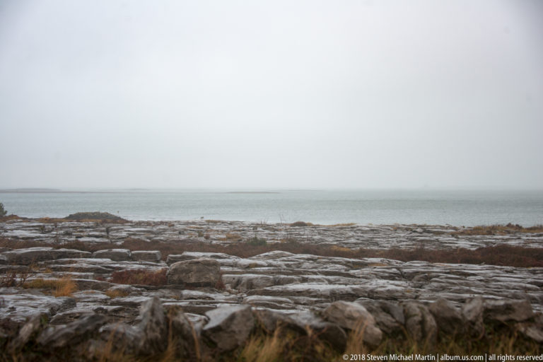 Low gray limestone shore stretching to a fog-softened Atlantic horizon beneath an overcast sky.