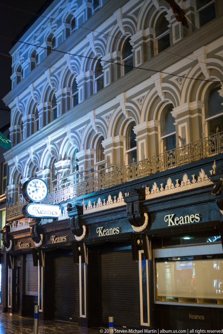 Ornate Keanes façade with repeated round arches, pale trim, balcony railings, and projecting clock signs.