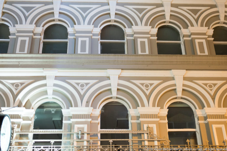Close view of stacked round arches, pilasters, pale trim, and balcony rail on an ornate historic façade.