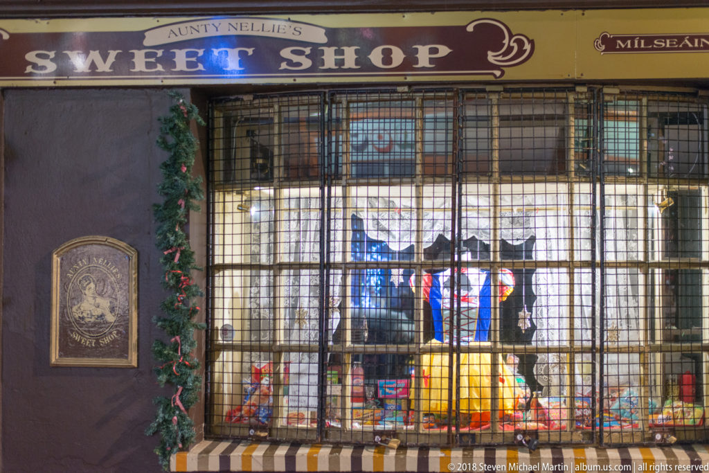 Traditional shop window with metal security grille, striped awning, fascia lettering, and merchandise inside.