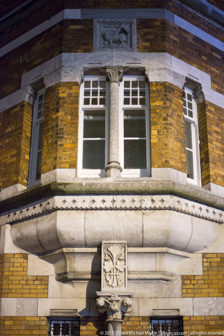 Curved stone bay on yellow-brick façade with sash windows, central column, and carved ornament.
