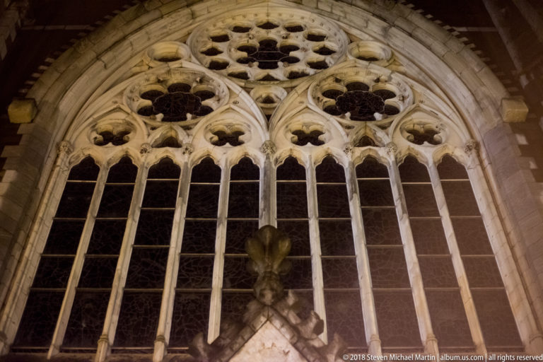 Tall Gothic pointed-arch window with stone tracery, lancets, quatrefoils, and dark glazing.