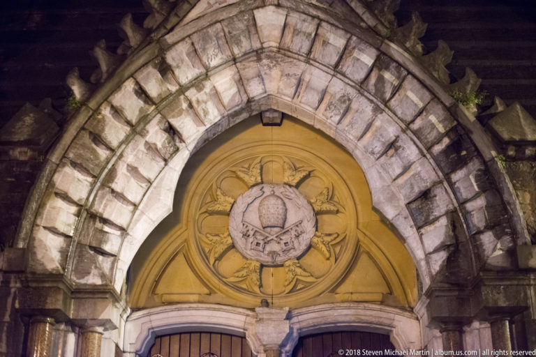Stone arched portal framing a yellow carved tympanum with scrolling relief and central medallion.