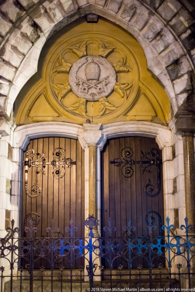 Twin wooden doors beneath yellow carved tympanum, framed by stone arch and iron railings.