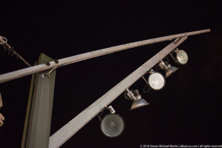 Angled metal lighting arm with several round and conical lamps silhouetted against the night sky.