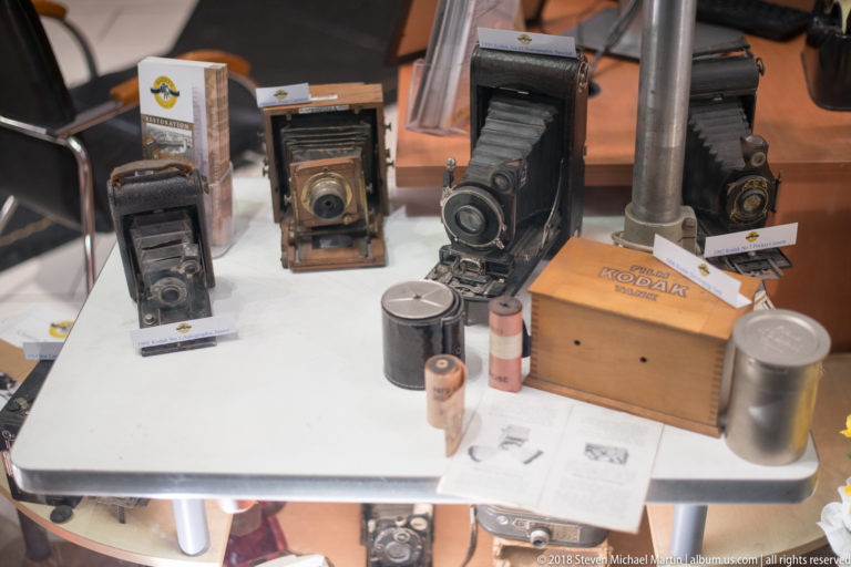Several vintage folding cameras displayed with Kodak packaging, film canisters, and photographic accessories on a tabletop.