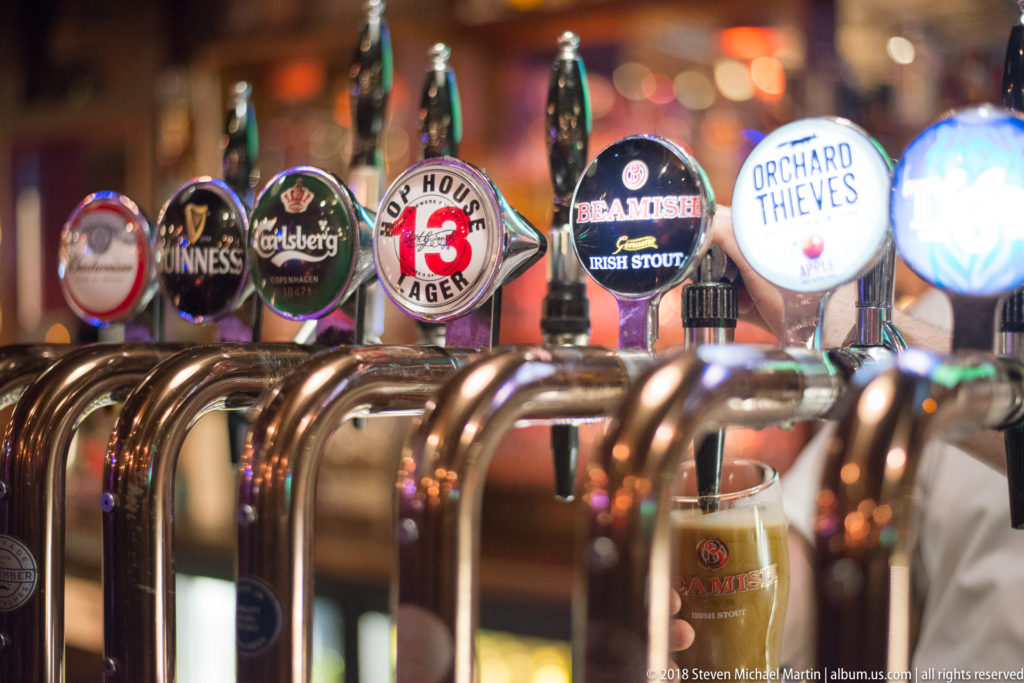 Row of chrome pub taps with Guinness, Beamish, Orchard Thieves, Hop House 13, and other branded badges.