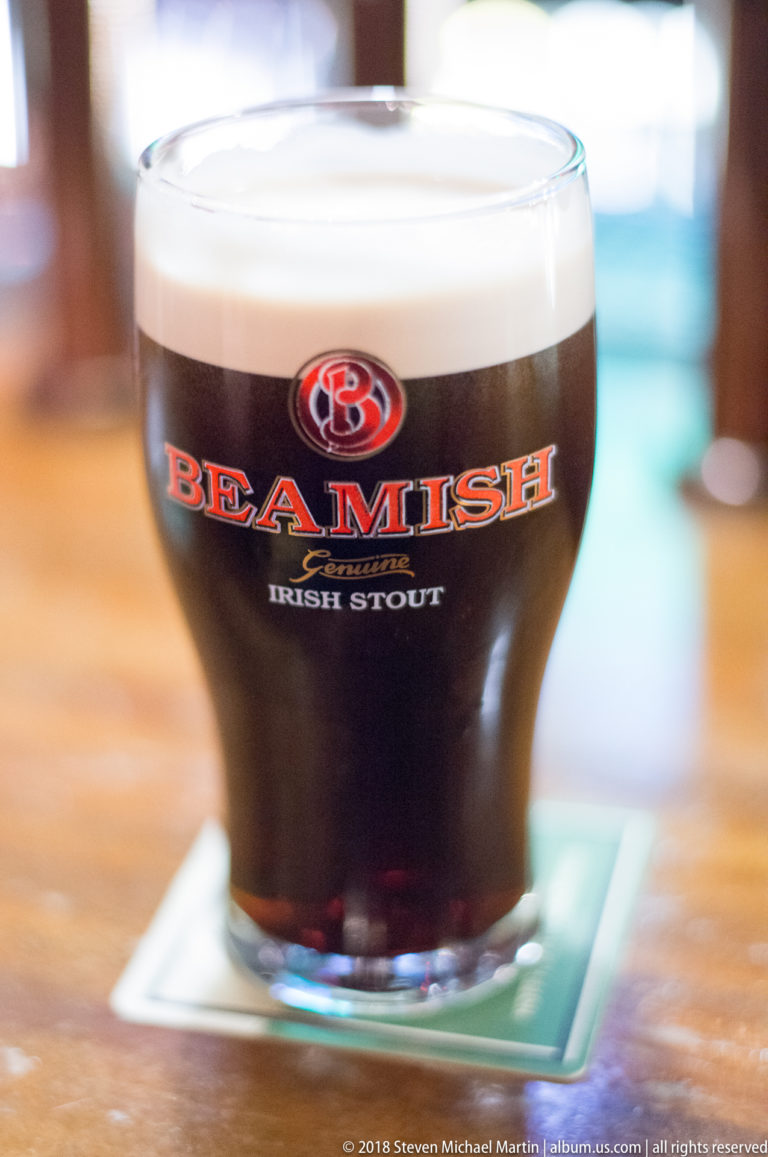 Close view of a pint of Beamish Irish Stout with a creamy head on a pub table.
