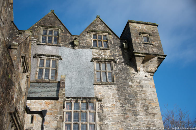 Close view of upper castle wall with steep gables, mullioned windows, render, and a projecting stone chamber.
