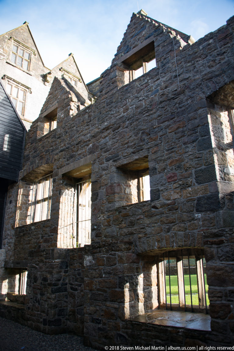 Roofless stone interior wall with rows of window openings and strong sunlight casting deep shadows.