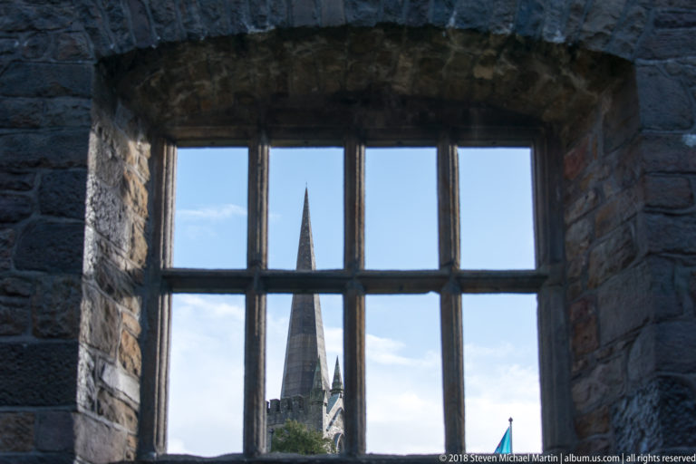 Church spire seen through a multi-pane castle window set in a deep stone reveal.