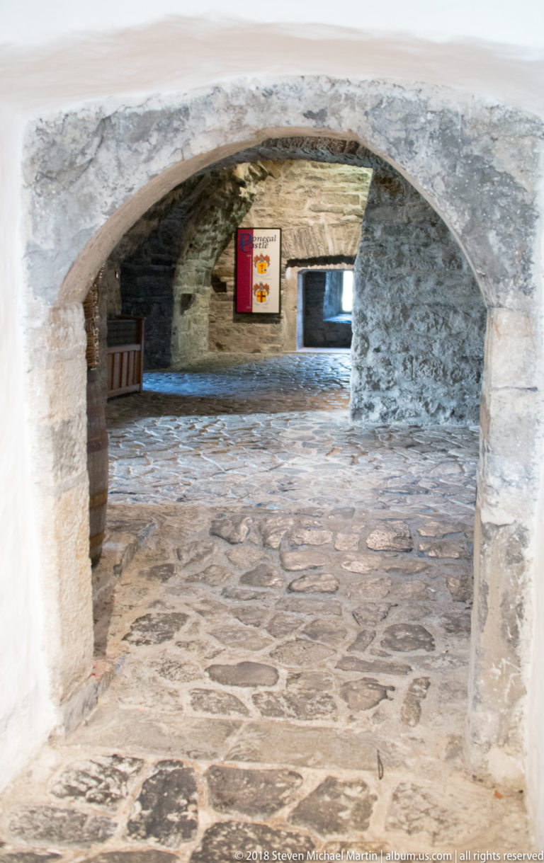 Broad low stone arch opening from a flagged room into another chamber with a display panel.