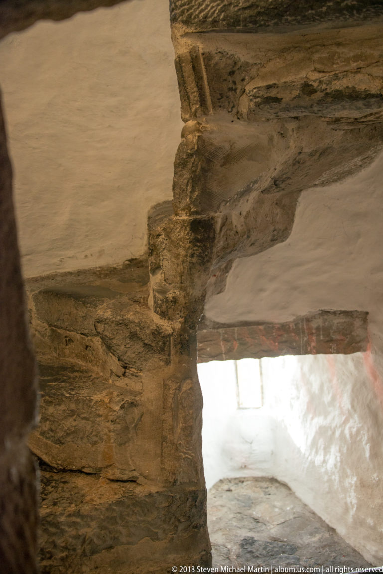 Close view of irregular stepped stone and plaster surfaces beside a bright wall opening.