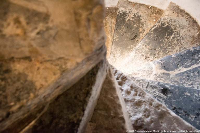 Close downward view of worn wedge-shaped stone stair treads turning through a tight stairwell.