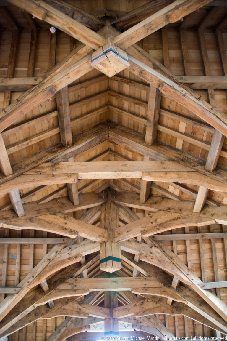Upward view of repeated timber roof trusses, rafters, and purlins beneath a pitched castle roof.