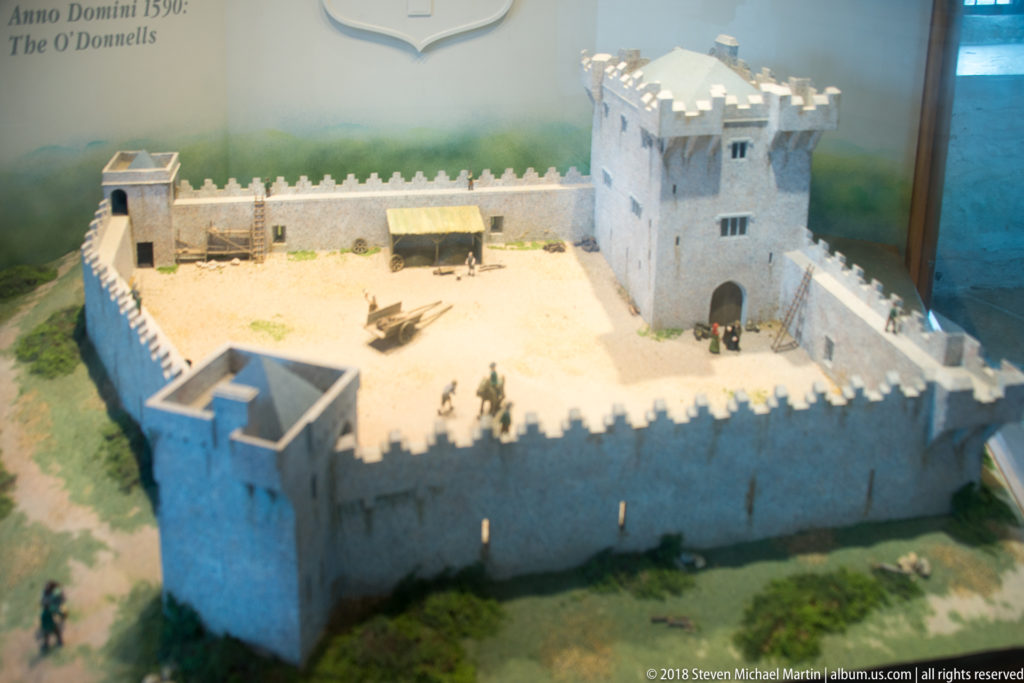 Oblique view of a castle scale model with crenellated walls surrounding a courtyard and a tall square tower.