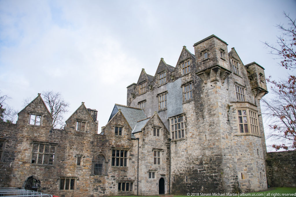 Oblique view of Donegal Castle across a lawn, showing a tall tower, clustered gables, projecting windows, and adjoining stone ranges.