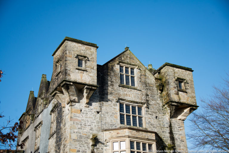Close upward view of twin projecting stone chambers flanking a gable with mullioned windows.