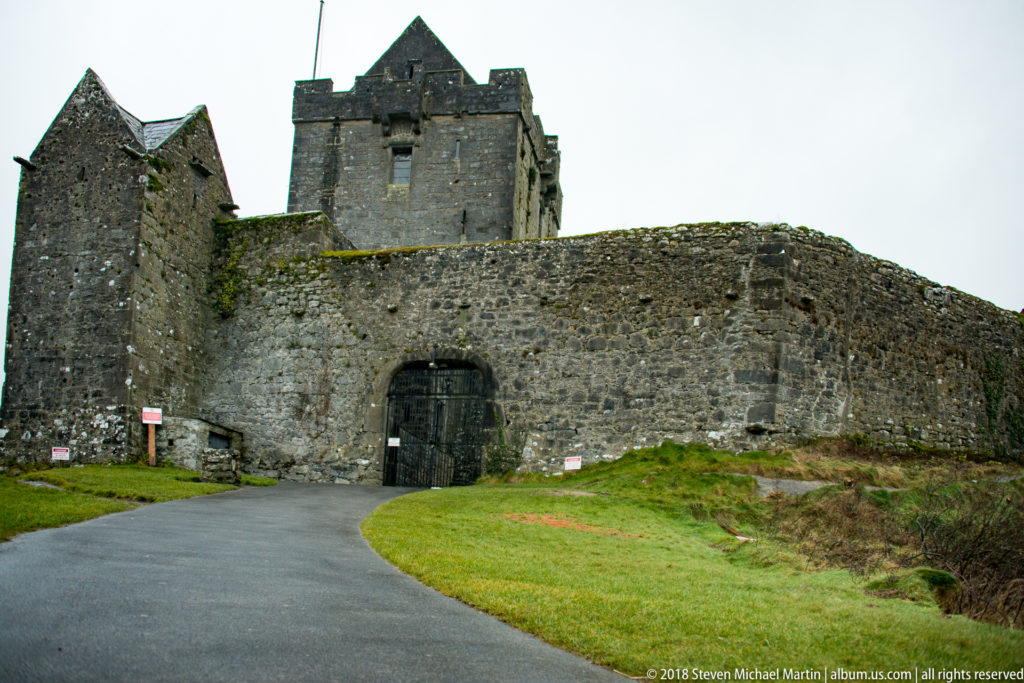 Close view of Dunguaire Castle’s arched gateway in a rough stone wall, with the tower house rising immediately behind.