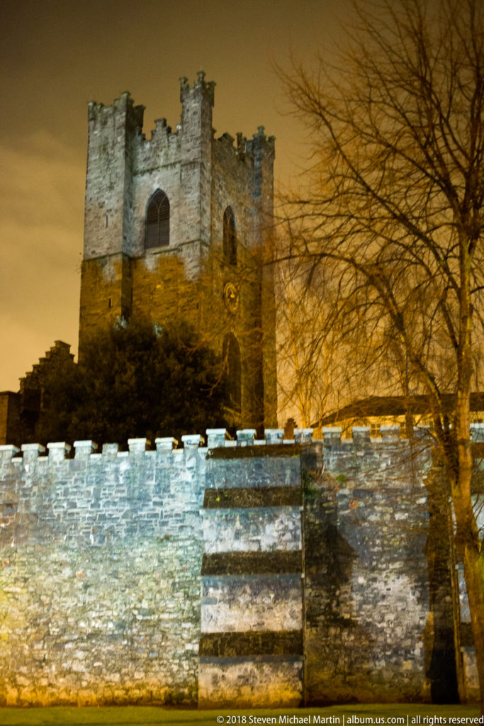 Floodlit Record Tower at Dublin Castle rising behind a crenellated stone wall and steps at night.