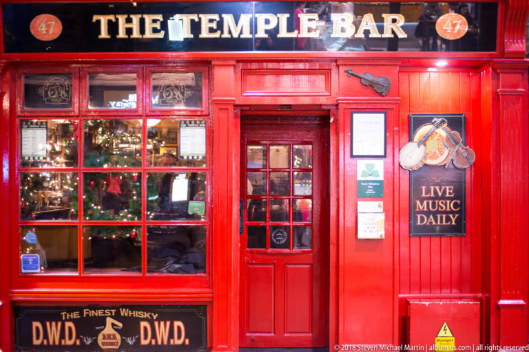 Bright red façade of The Temple Bar pub with paneled door, multi-paned windows, whisky lettering, and live-music sign.