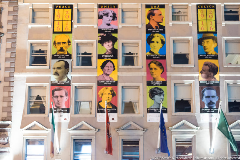 Building façade covered with portrait banners commemorating figures associated with 1916, with Irish flags below.