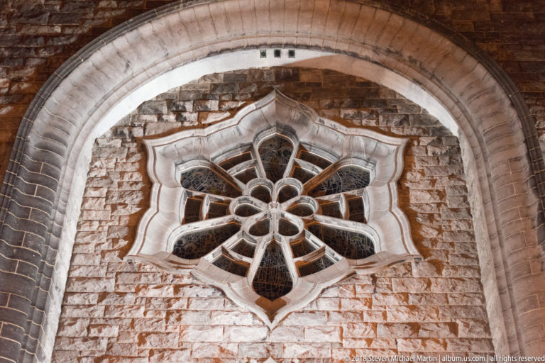 Flower-shaped tracery window set within a large pointed stone arch on Galway Cathedral at night.