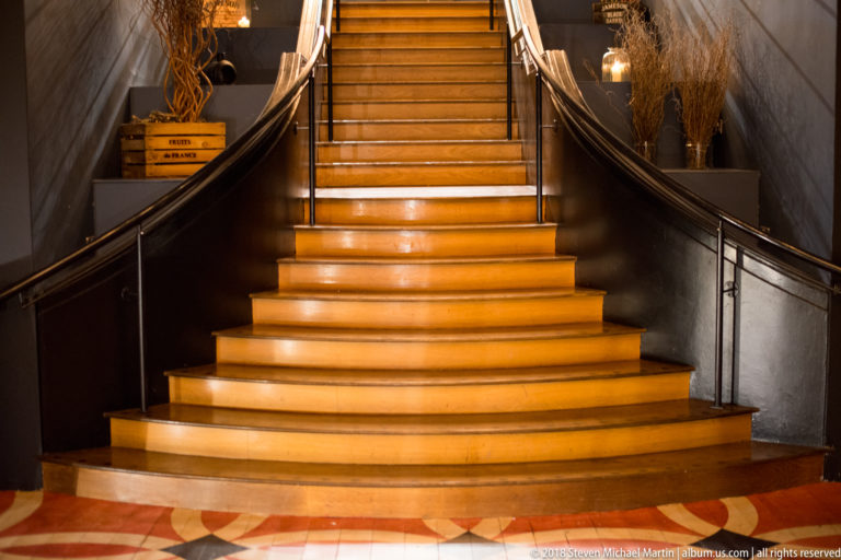 Broad glowing staircase with pale steps, dark curved handrails, and warm concealed lighting in a formal interior.