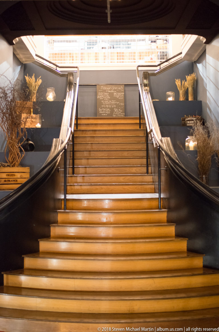 Symmetrical illuminated staircase rising to a bright landing, with curved handrails and decorative arrangements along dark walls.