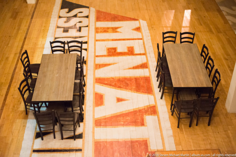 Overhead view of restaurant tables and chairs arranged beside a bold red-and-white painted graphic on a wooden floor.