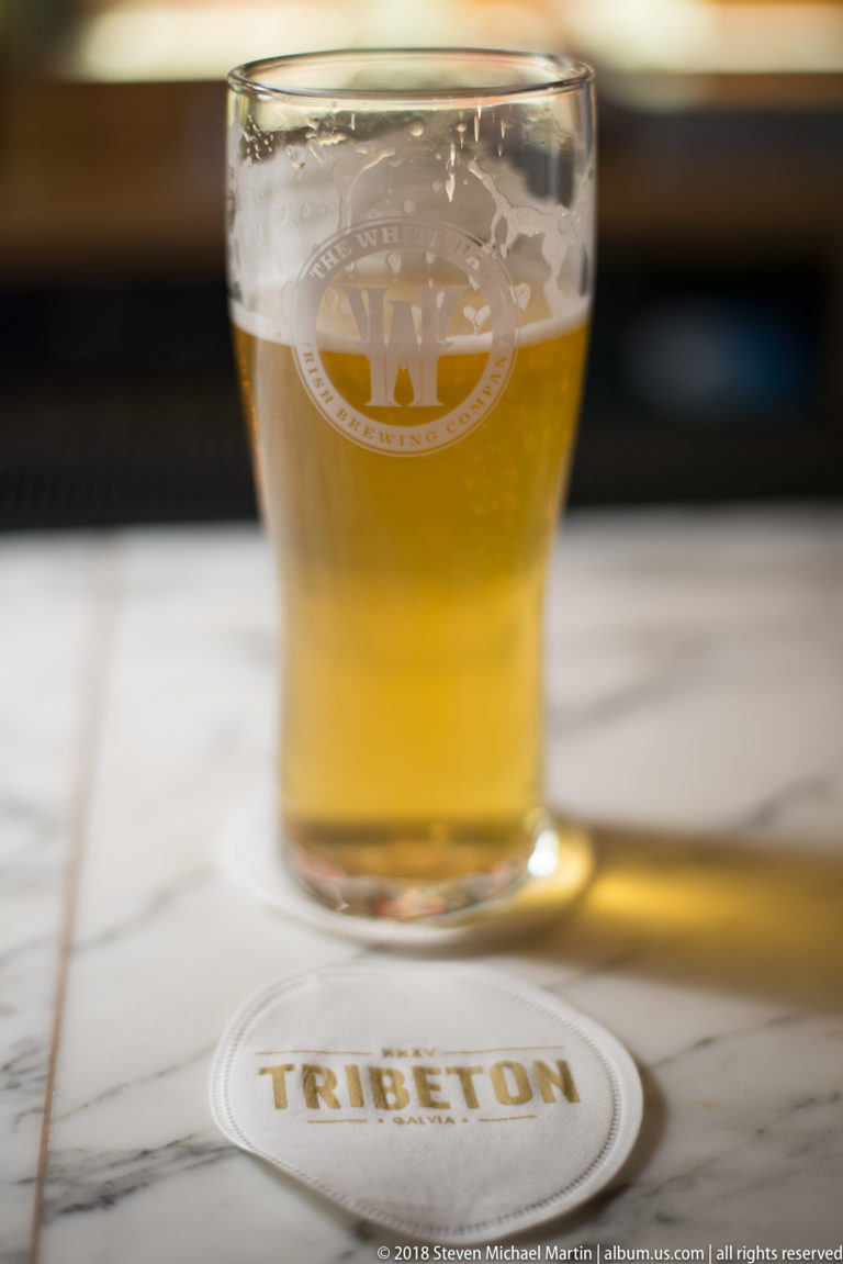 Partly consumed glass of pale beer on a marble bar beside a coaster marked TRIBETON.